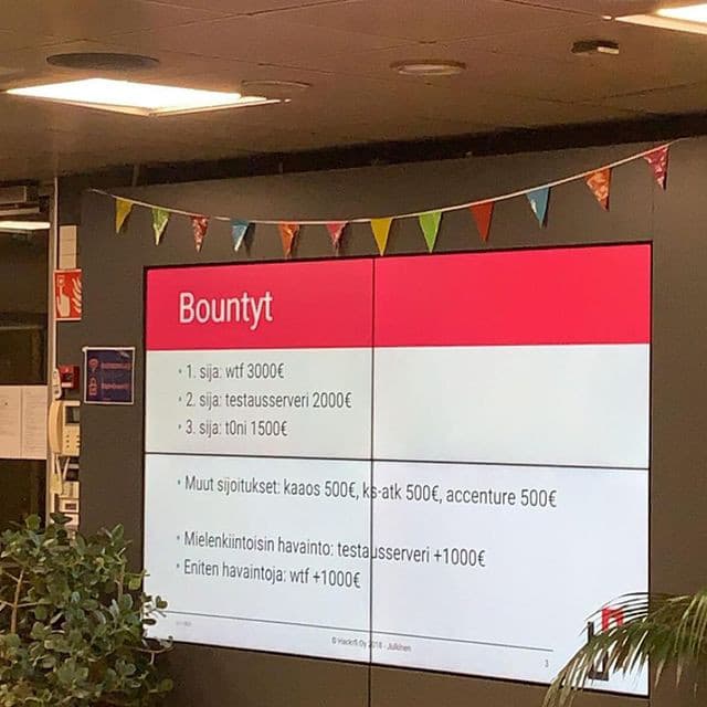 Valokuva LähiTapiola Hack Day -tapahtumasta. Seinälle heijastettu kuva, jossa teksti: "Bountyt. // - 1. sija: wtf 3000€ // - 2. sija: testausserveri 2000€ // - 3. sija: t0ni 1500€ // - Muut sijoitukset: kaaos 500€, ks-atk 500€, accenture 500€ // Mielenkiintoisin havainto: testausserveri +1000€ // - Eniten havaintoja: wtf +1000€